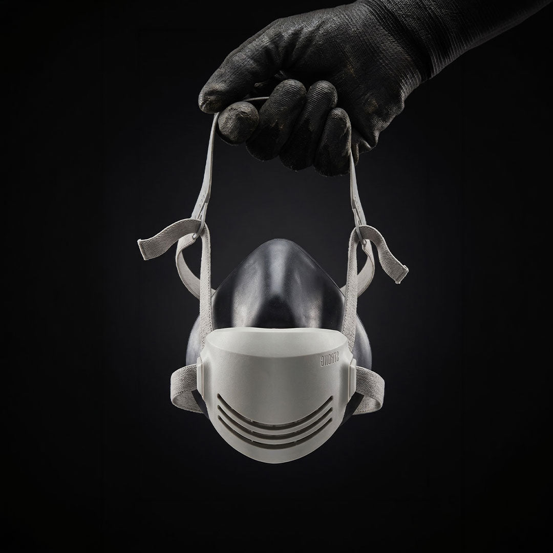 Hand wearing a black glove holding a white face mask against a black background