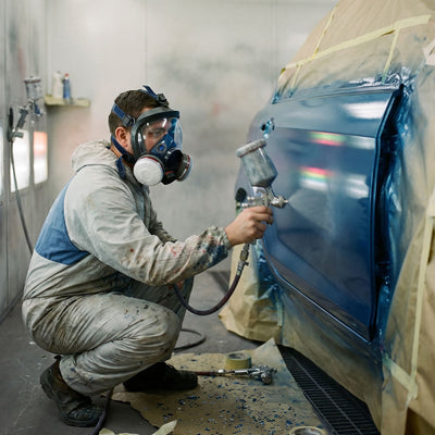 Person spray painting a car in a controlled environment