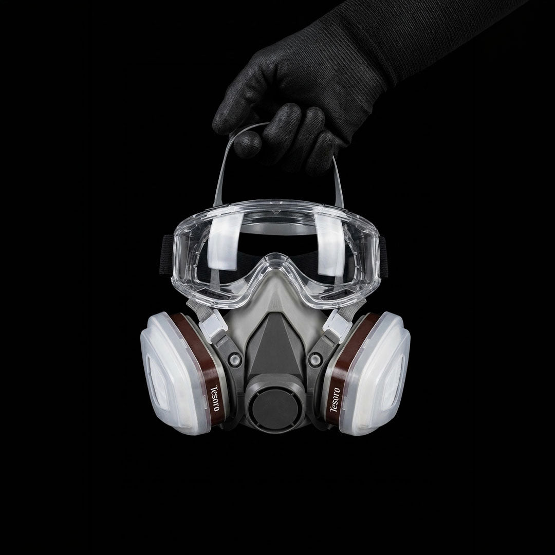Respirator mask with goggles held by a gloved hand on a black background