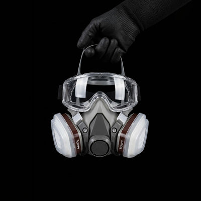 Respirator mask with goggles held by a gloved hand on a black background
