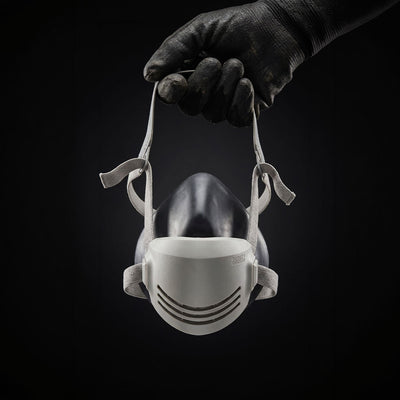 Hand wearing a black glove holding a white face mask against a black background