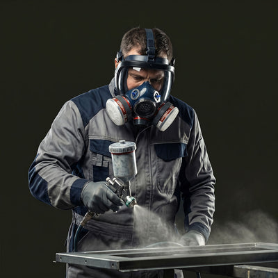 Person wearing a protective suit and mask using a spray gun on a dark background